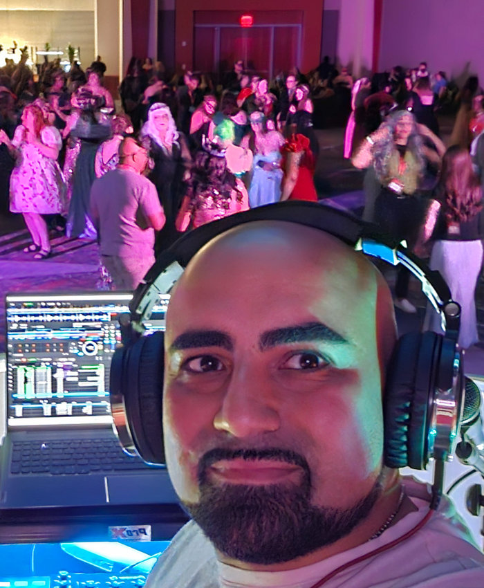 Alex wearing headphones at his booth, with a packed dance floor behind him