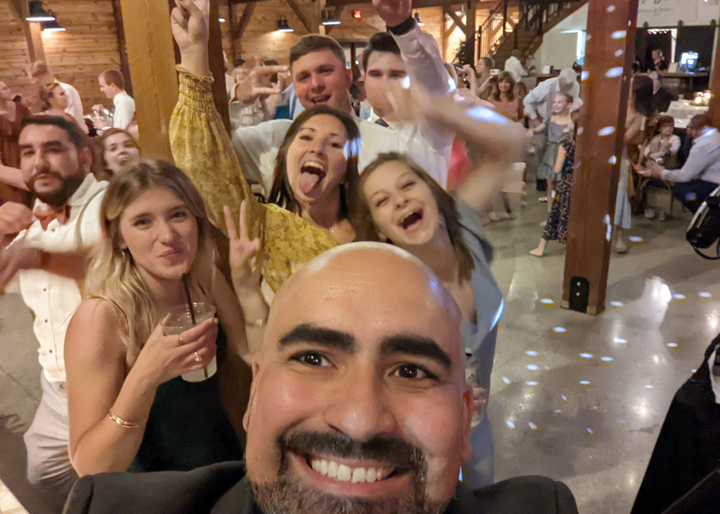 Alex taking a selfie with cheering wedding guests in a barn